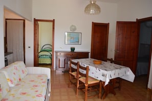 A cozy living room with a sofa, a dining table with chairs, a wooden cabinet, and a painting on the wall. - THREE-ROOM APARTMENT BADAS Costa Rei Centro (Costa Rei)