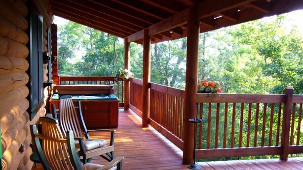 Une terrasse en bois, agrémentée de fauteuils à bascule et d’une table, entourée d’une balustrade en bois et d’une végétation luxuriante.