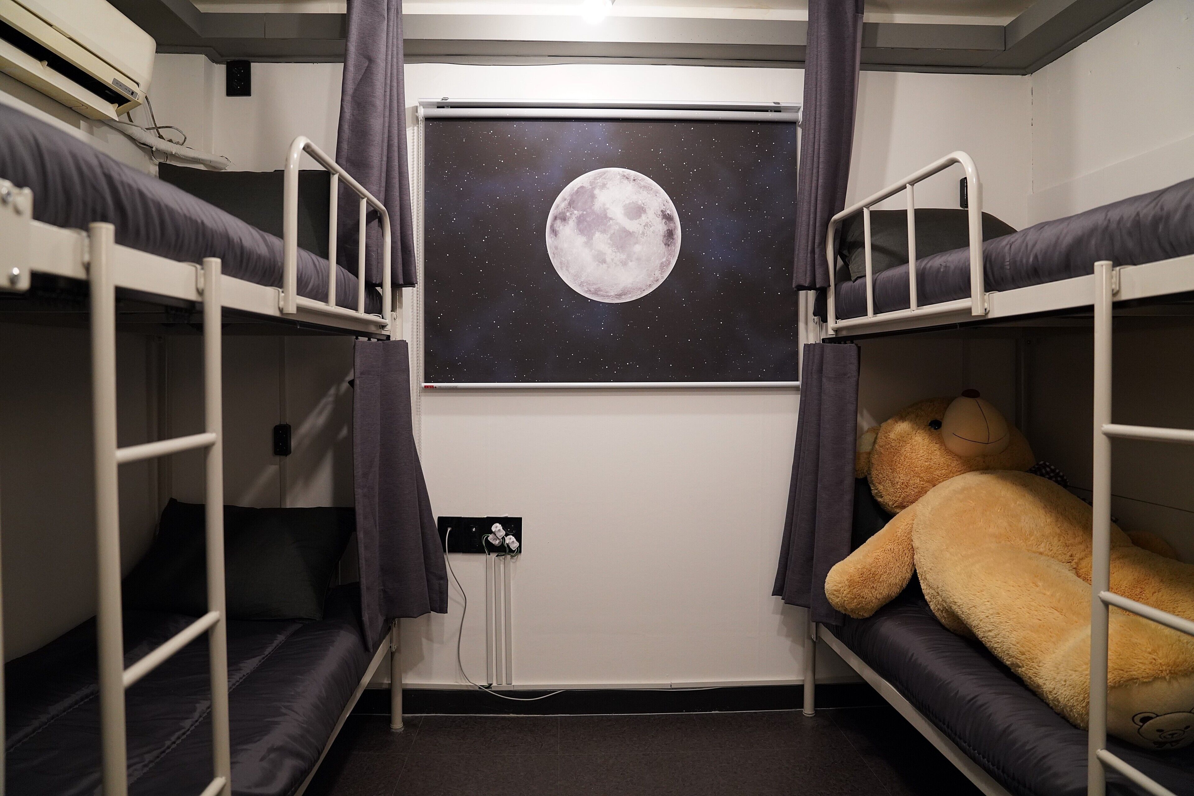 Dormitorio con literas, dos camas, un cartel grande con forma de luna en la pared y un osito de peluche en una de las camas.