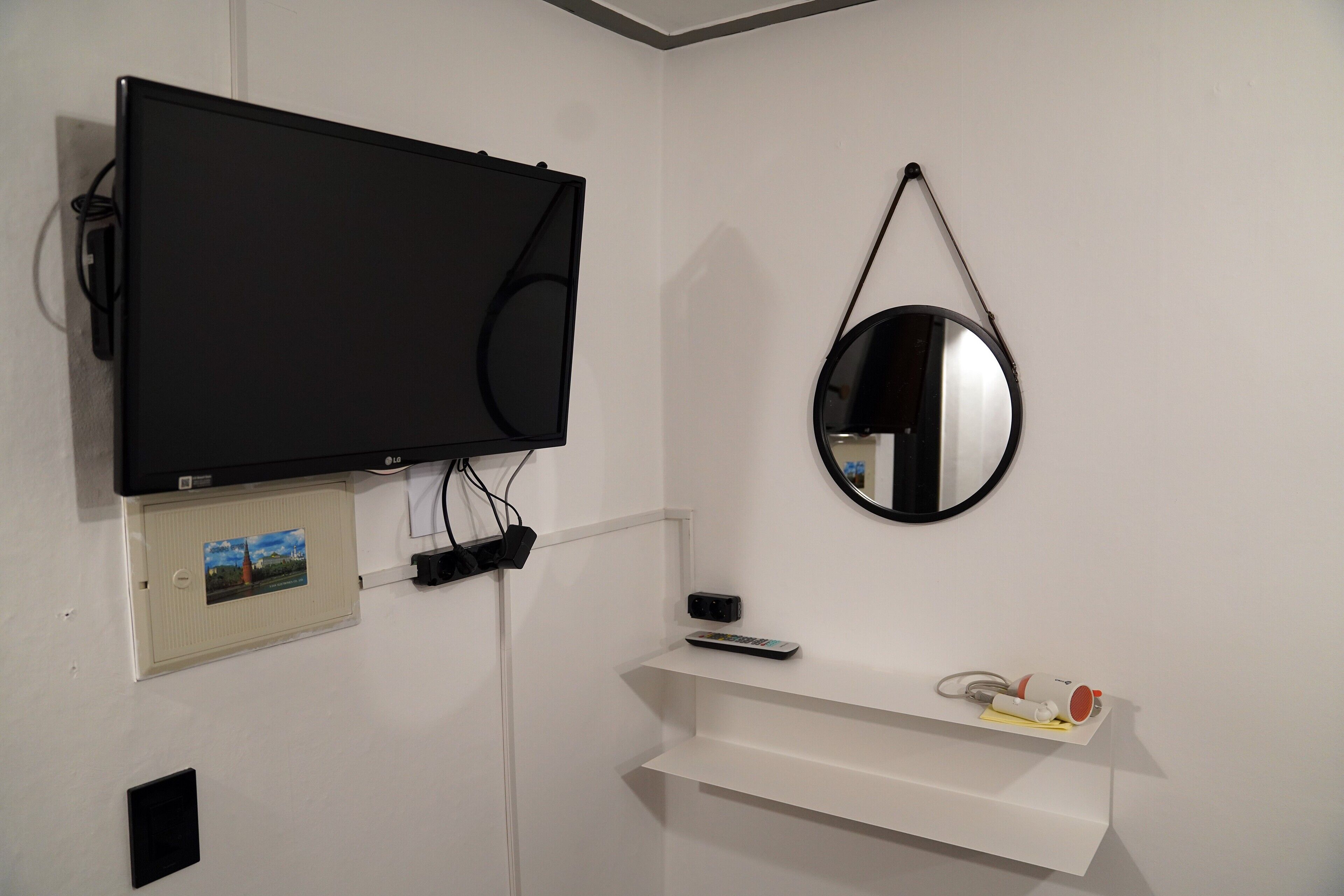 A room with a mounted TV, a wall-mounted mirror, a shelf with a remote control, and a picture frame.