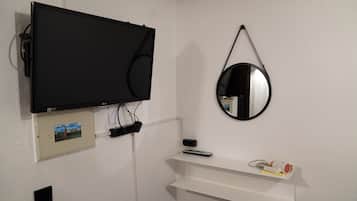 A room with a mounted TV, a wall-mounted mirror, a shelf with a remote control, and a picture frame.