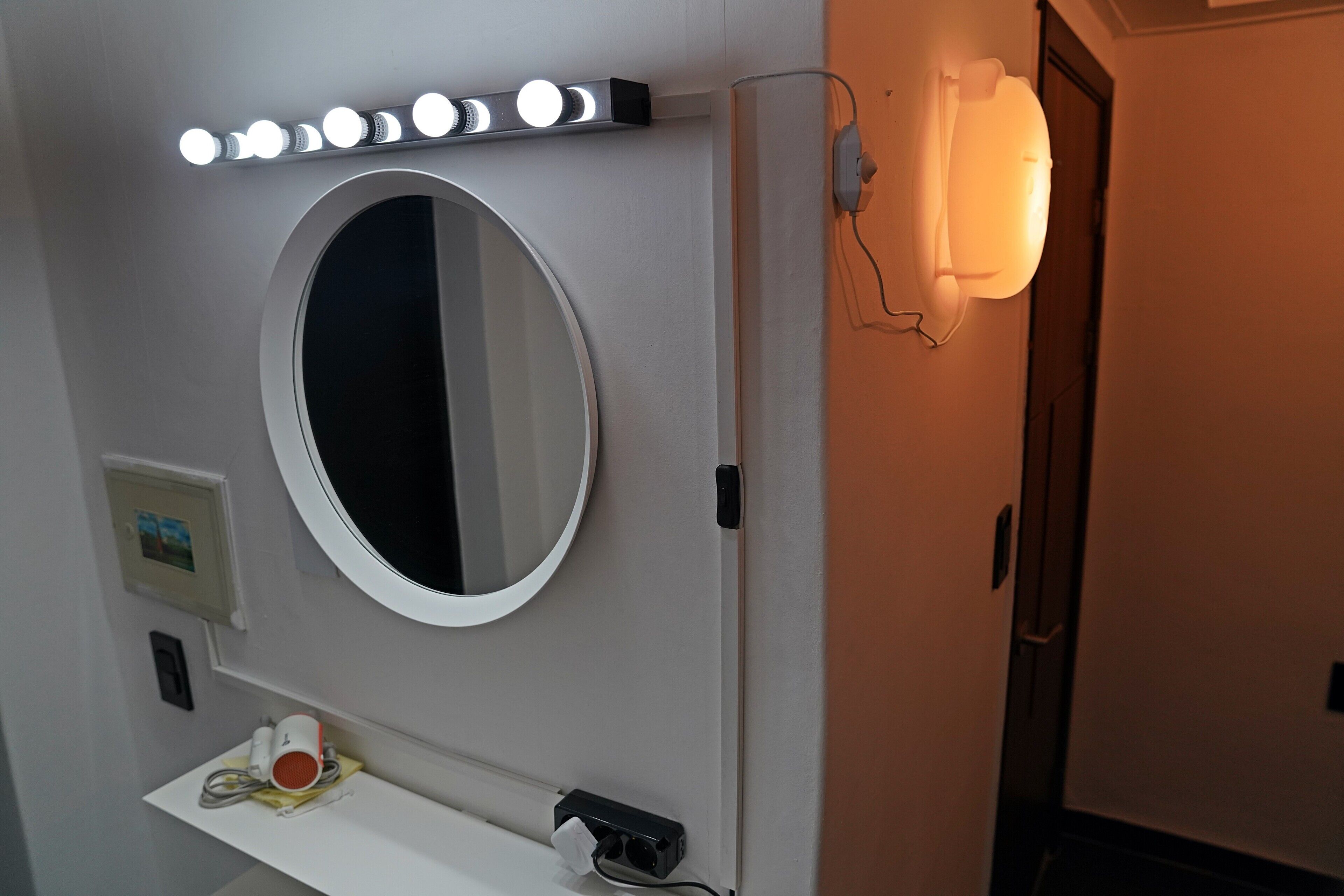 A bathroom with a round mirror, a vanity with a cup and a tissue, and a wall-mounted light fixture.