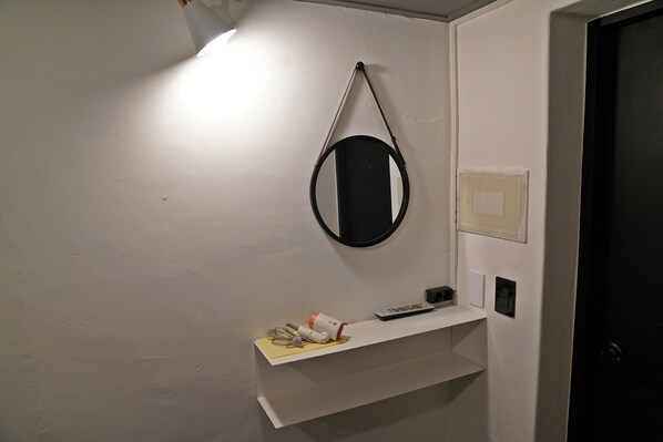 Un mur blanc orné d’un miroir, une étagère avec une télécommande et une porte.