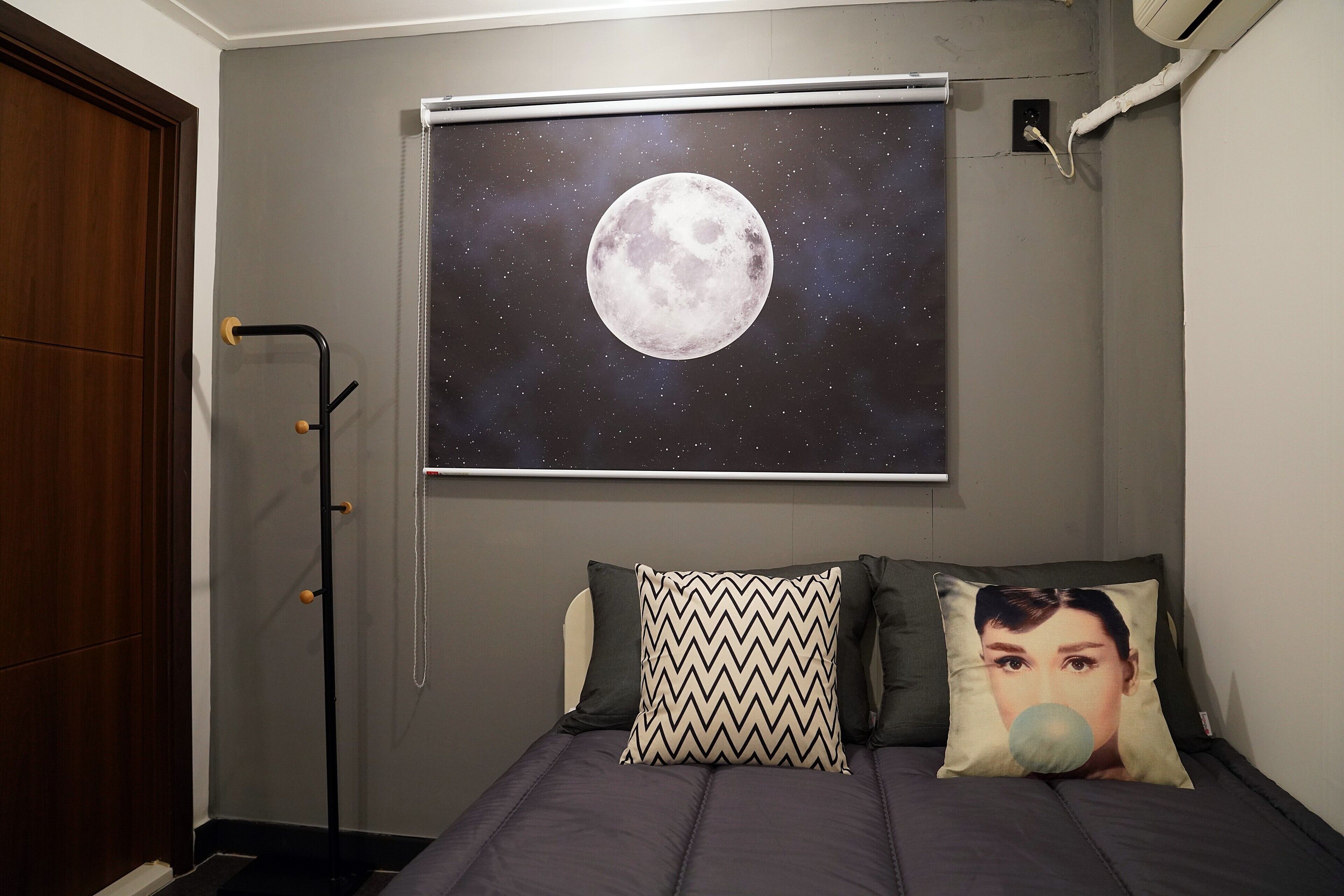 Un dormitorio con cama, televisor montado en la pared mostrando una luna y una puerta.