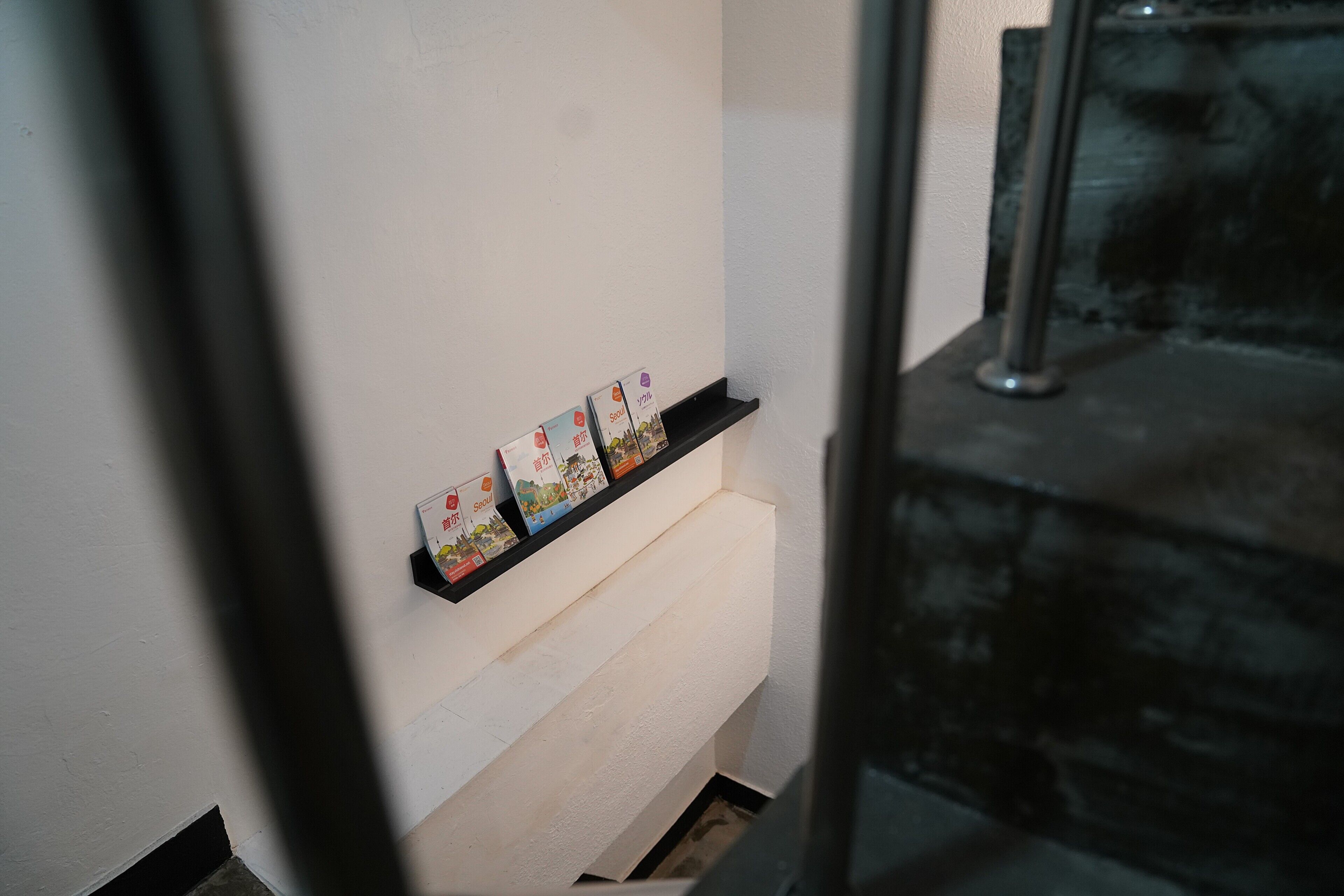 Een gang met een witte muur en een zwarte plank waarop enkele boeken staan.