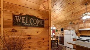 Un interior de madera con un cartel que dice 'WELCOME family & friends', una zona de comedor con mesa y sillas, y una cocina equipada.