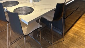 A modern kitchen with a marble countertop, black chairs, a glass dining table, and a built-in stove.