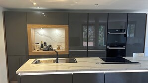 A modern kitchen with a marble countertop, built-in appliances, and a wooden-framed mirror.
