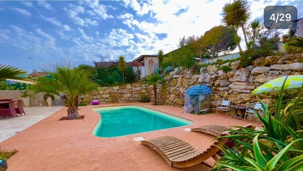 A swimming pool with lounge chairs, surrounded by a stone wall and greenery.