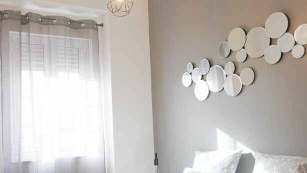Una cama bien hecha con una toalla enrollada, una lámpara colgante y una pared con espejos circulares.
