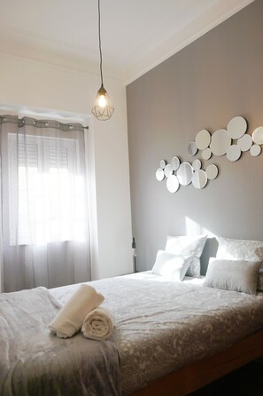 Una cama bien hecha con una toalla enrollada, una lámpara colgante y una pared con espejos circulares.