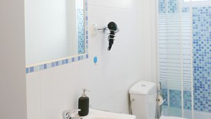 Un baño con lavamanos blanco, un espejo, inodoro y zona de ducha.