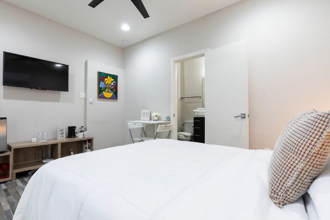 A modern hotel room with a large bed, a desk, a chair, a flat-screen TV, and a painting on the wall.