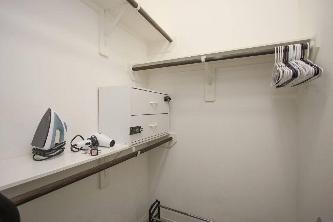 Una habitación pequeña y limpia con un planchador blanco, un secador de pelo y un toallero con toallas dobladas.
