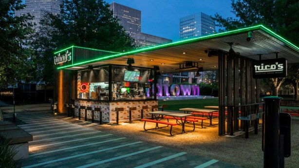 En restaurant med udendørs siddepladser, et neon-skilt og udsigt til byens skyline.