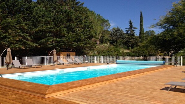 Ein rechteckiger Swimmingpool mit Holzdeck, umgeben von einem weißen Zaun und beschattet durch Sonnenschirme.