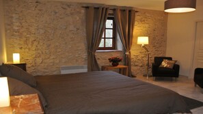 Ein Schlafzimmer mit Steinsturz, einem Bett, einem Nachttisch mit Lampe, einem Sessel und einem kleinen Tisch mit Blumen.