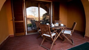 A patio with a table set for two, wooden chairs, and a sliding glass door leading to a garden.
