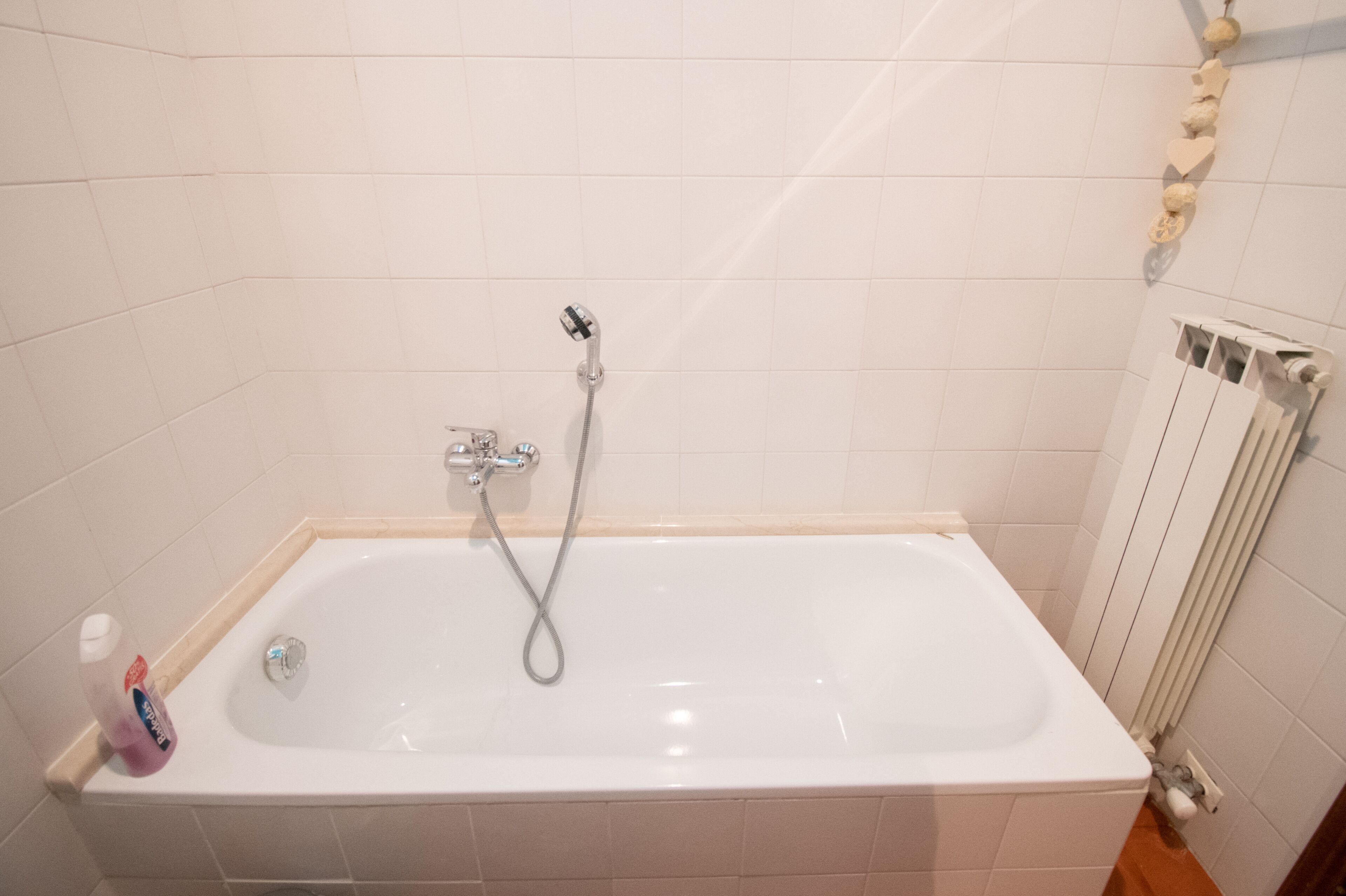A white bathtub with a handheld showerhead, a bottle of shampoo, and a towel rack with a towel.