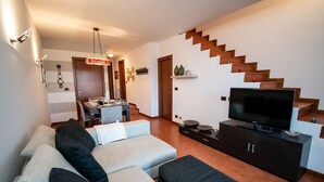 A living room with a sofa, a TV on a cabinet, and a staircase.