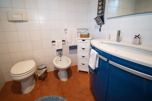 Een badkamer met toilet, bidet en een blauwe wastafel met spiegel.
