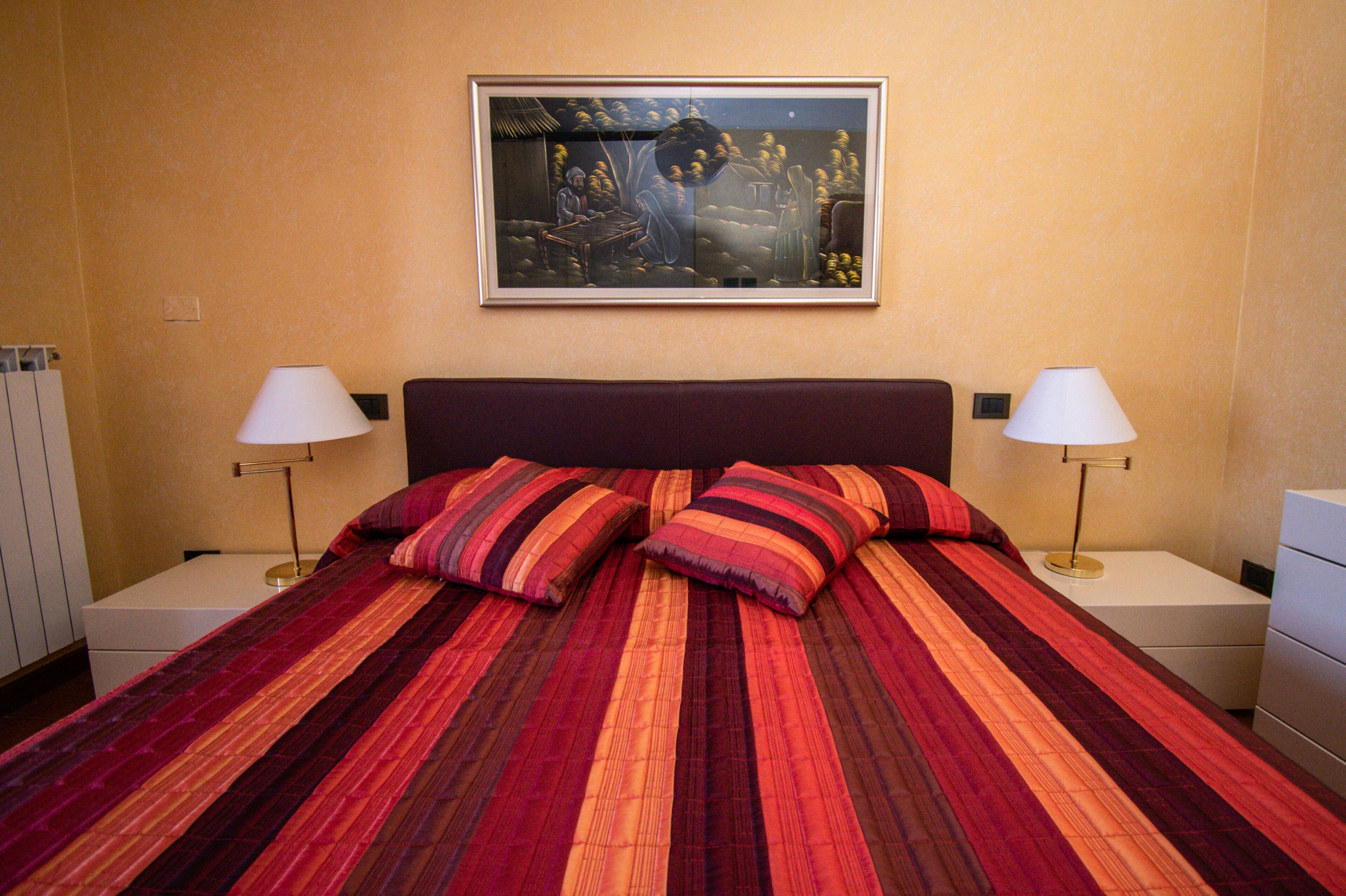 A hotel room with a large bed, two bedside tables with lamps, a framed artwork on the wall, and a nightstand with a lamp.