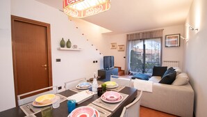A dining area with a table set for four, a sofa, a television, and a staircase leading to another level.