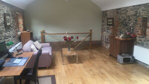 Un salon chaleureux avec un plancher en bois, un mur en pierre, un escalier en bois, un canapé, une table basse et un bureau avec un ordinateur.