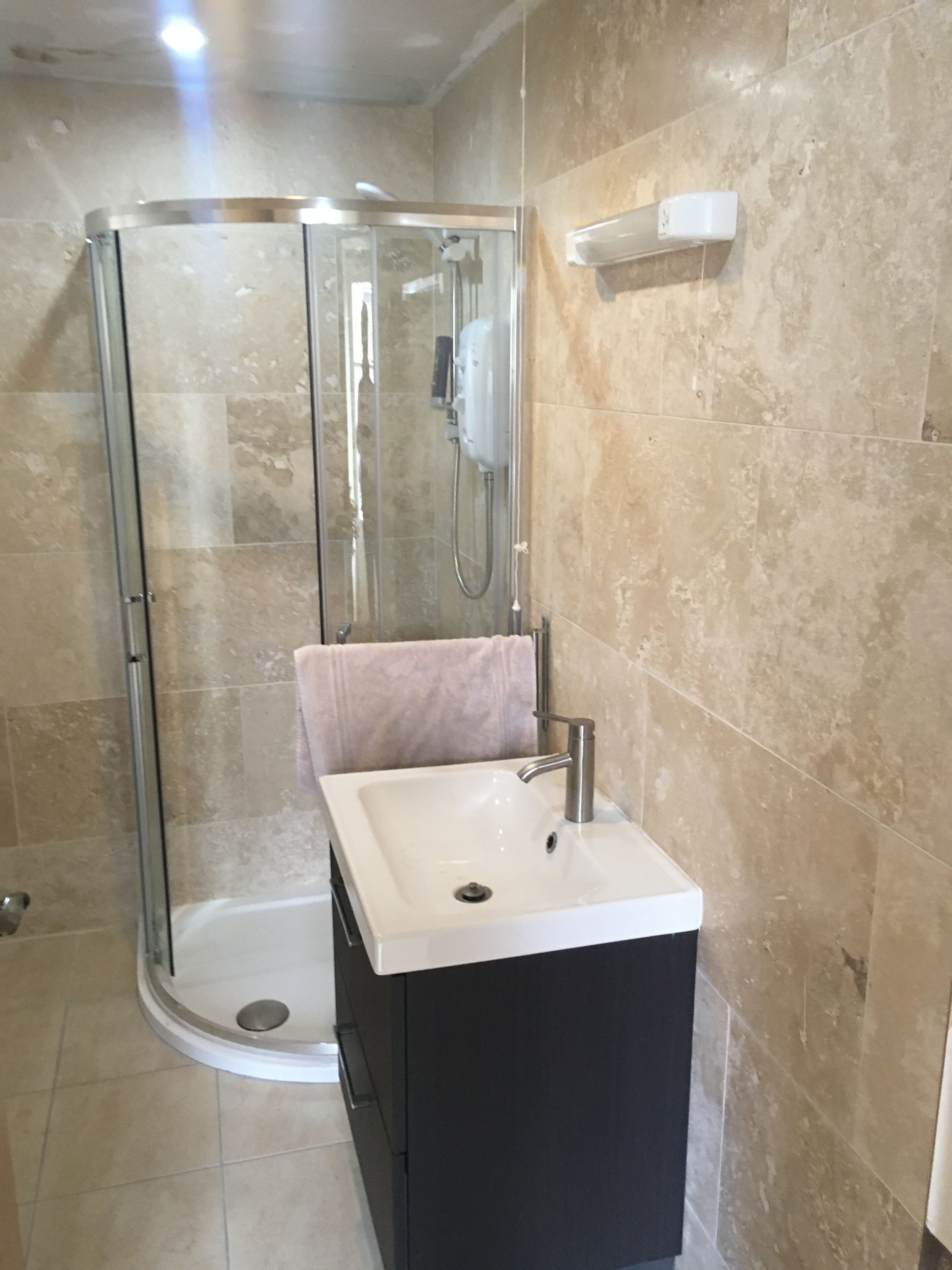 A bathroom with a glass-enclosed shower, a sink with a black cabinet, and beige tiled walls.