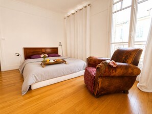 A bedroom with a wooden bed, a wooden nightstand, a brown leather armchair, and a window with curtains.