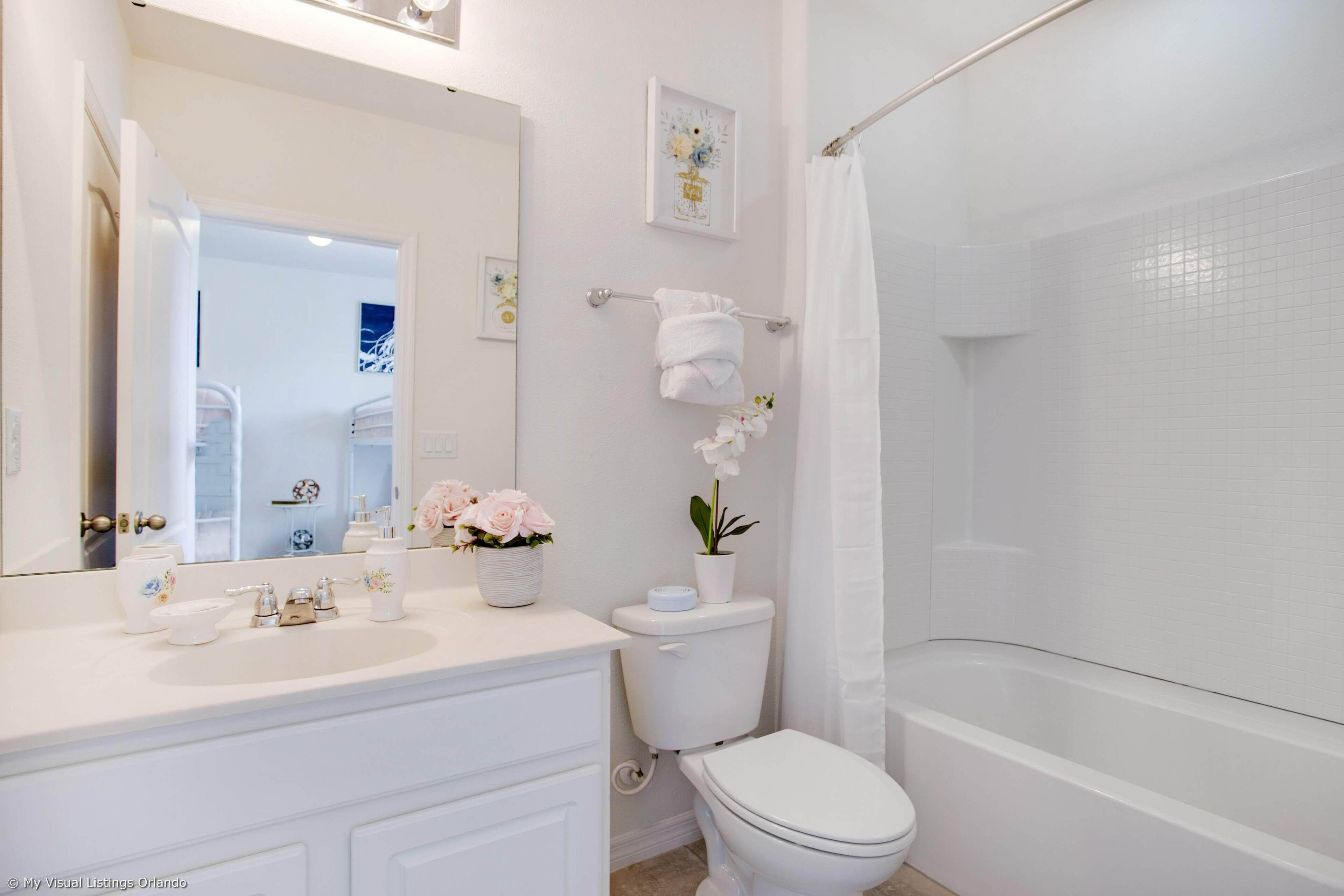A bathroom with a white sink, toilet, and bathtub. There are decorative items like flowers and a framed picture on the wall.