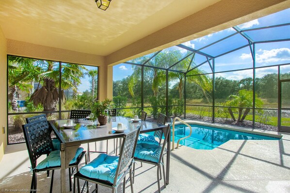 A glass-enclosed patio with a pool, outdoor seating, and a view of the surrounding greenery.