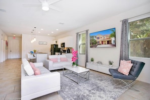A modern living room with a white sofa, a grey armchair, and a coffee table. There is a kitchen area in the background with white cabinets and a dining table. - Enjoy the Private View! Roomy Town Home With Pool, 20 Mins From Disney #5st739 (Davenport)