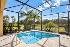 An indoor swimming pool with a view of palm trees and a clear sky through large windows.