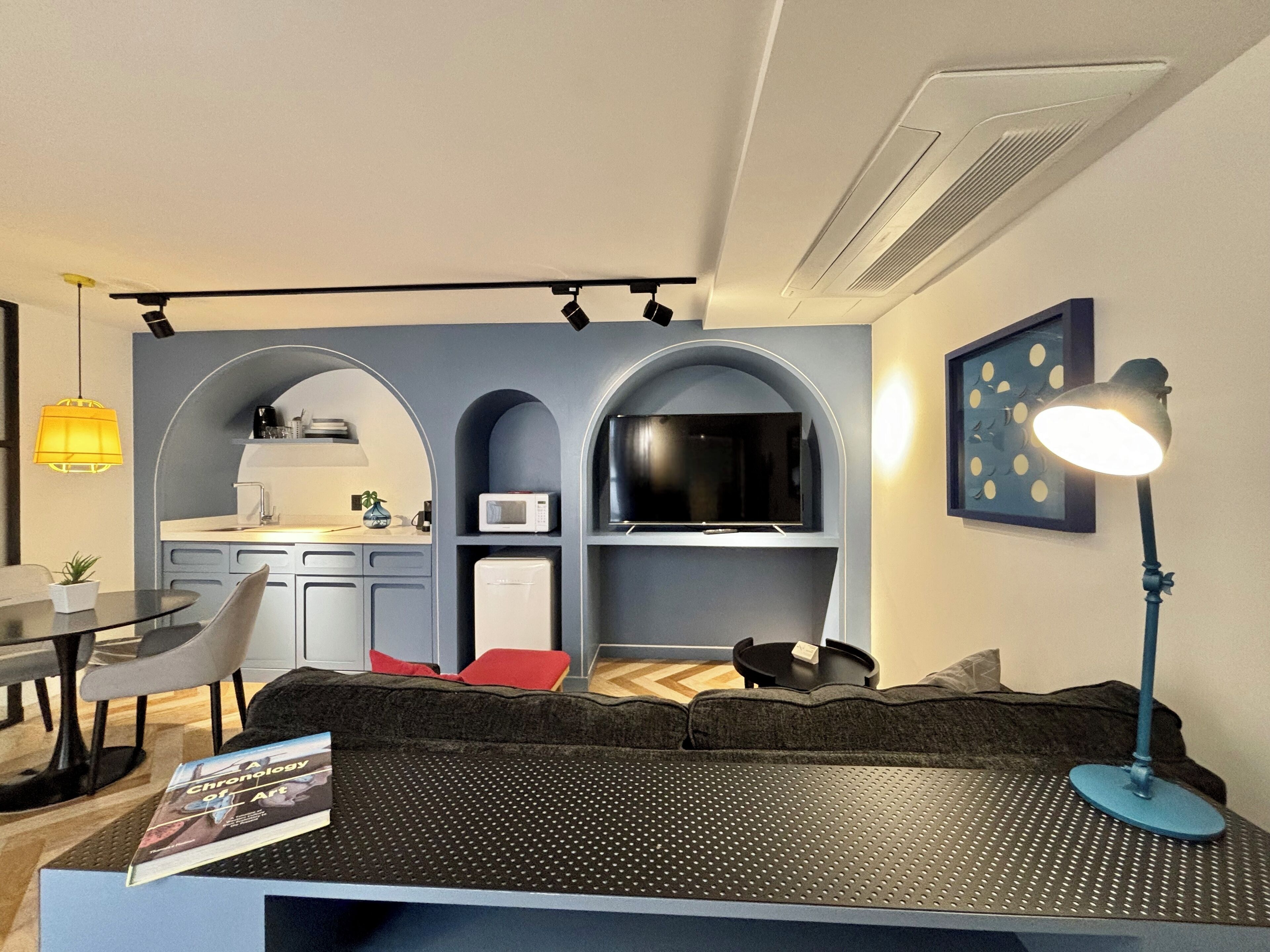 A compact living space with a kitchenette, a sofa, a dining area, and a reading area with a book.