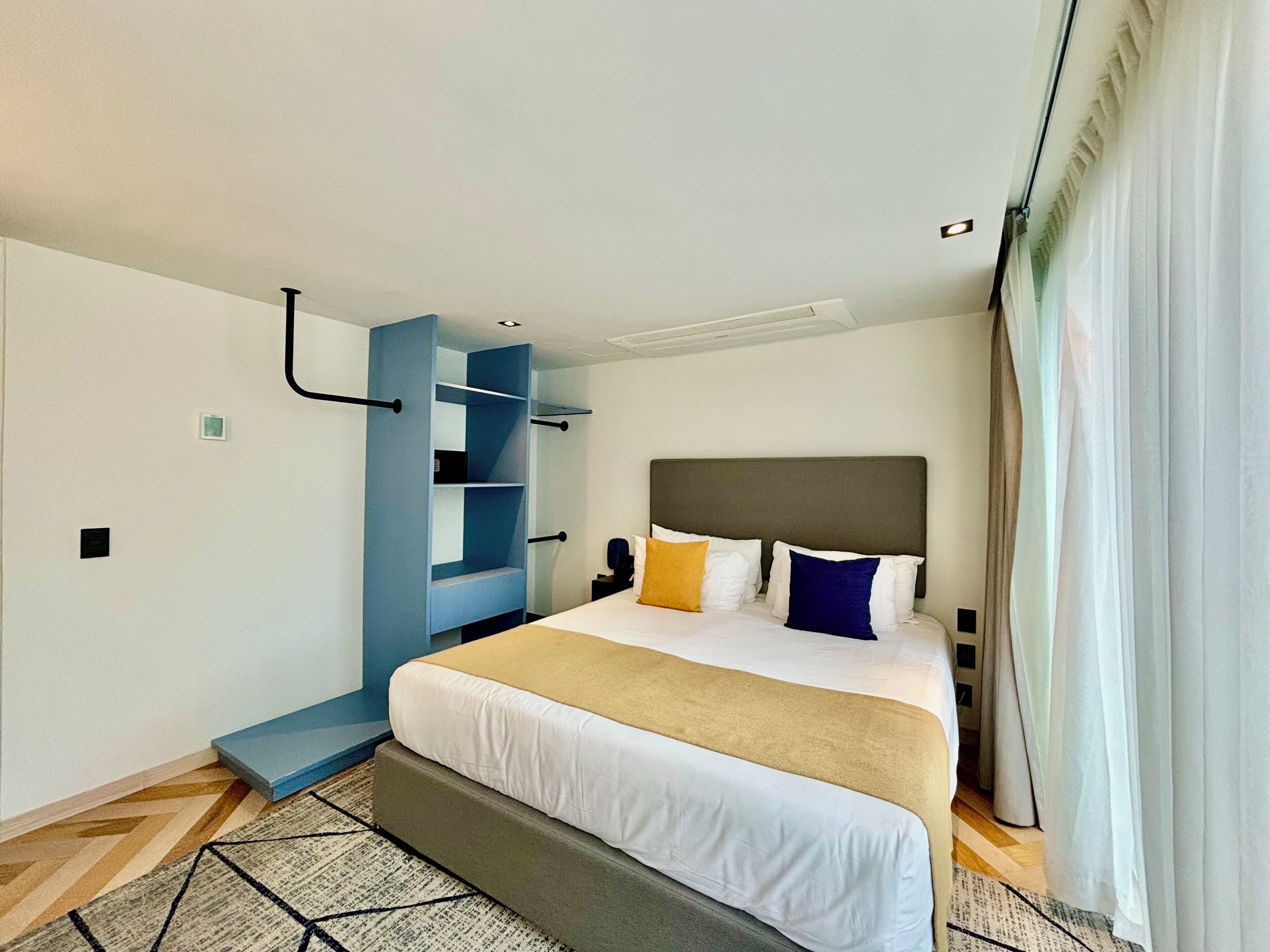 A modern hotel room with a large bed, a built-in wardrobe, and a view of the city.