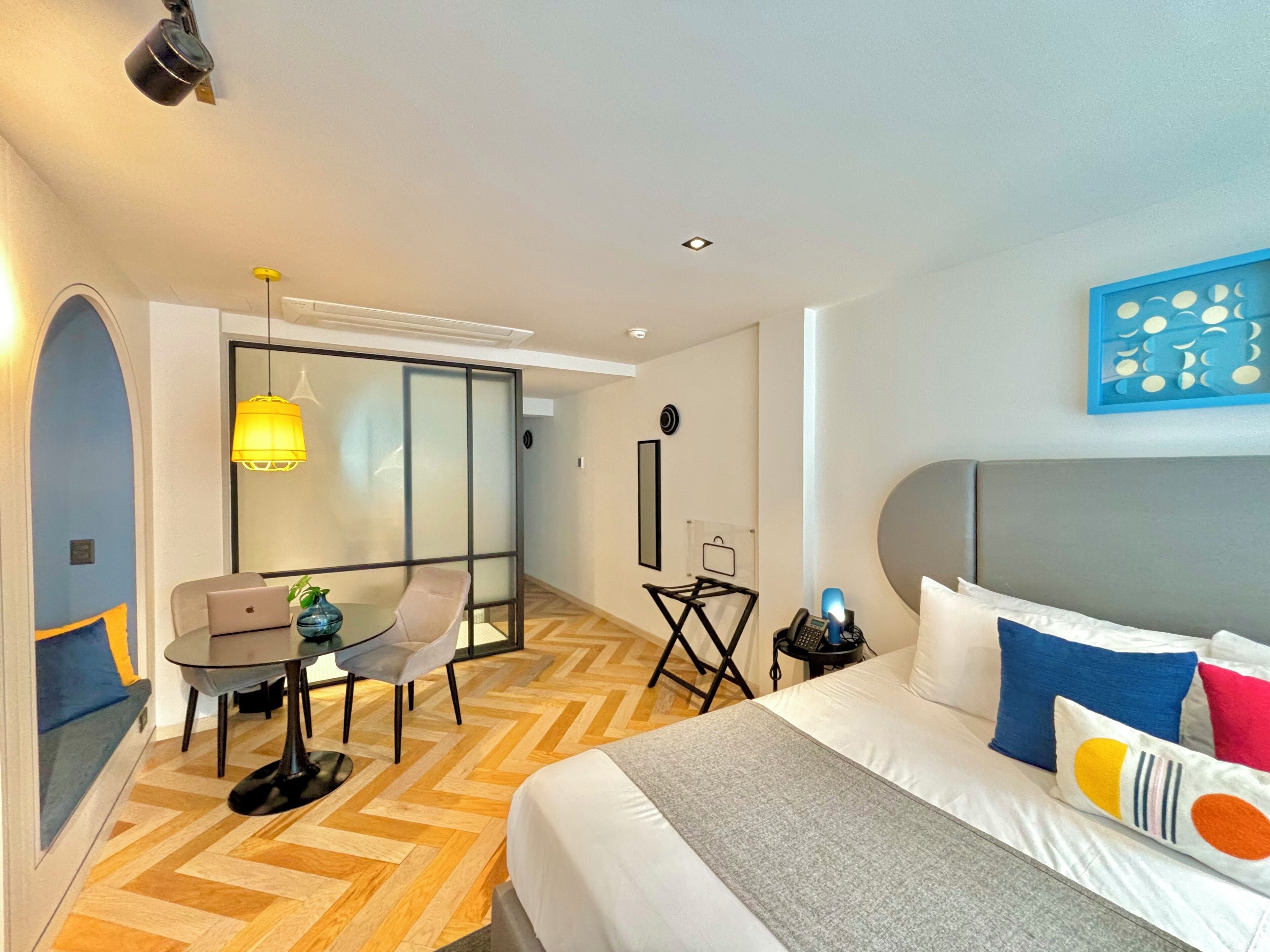Una habitación de hotel moderna con una cama grande, un escritorio con una computadora portátil, una silla y una pequeña mesa con una planta.