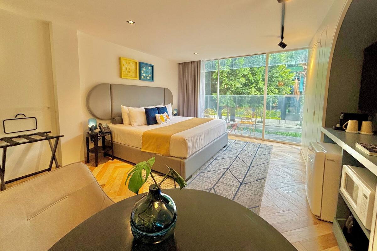 Habitación de hotel con cama, escritorio, silla, mesa de comedor y vista al exterior.