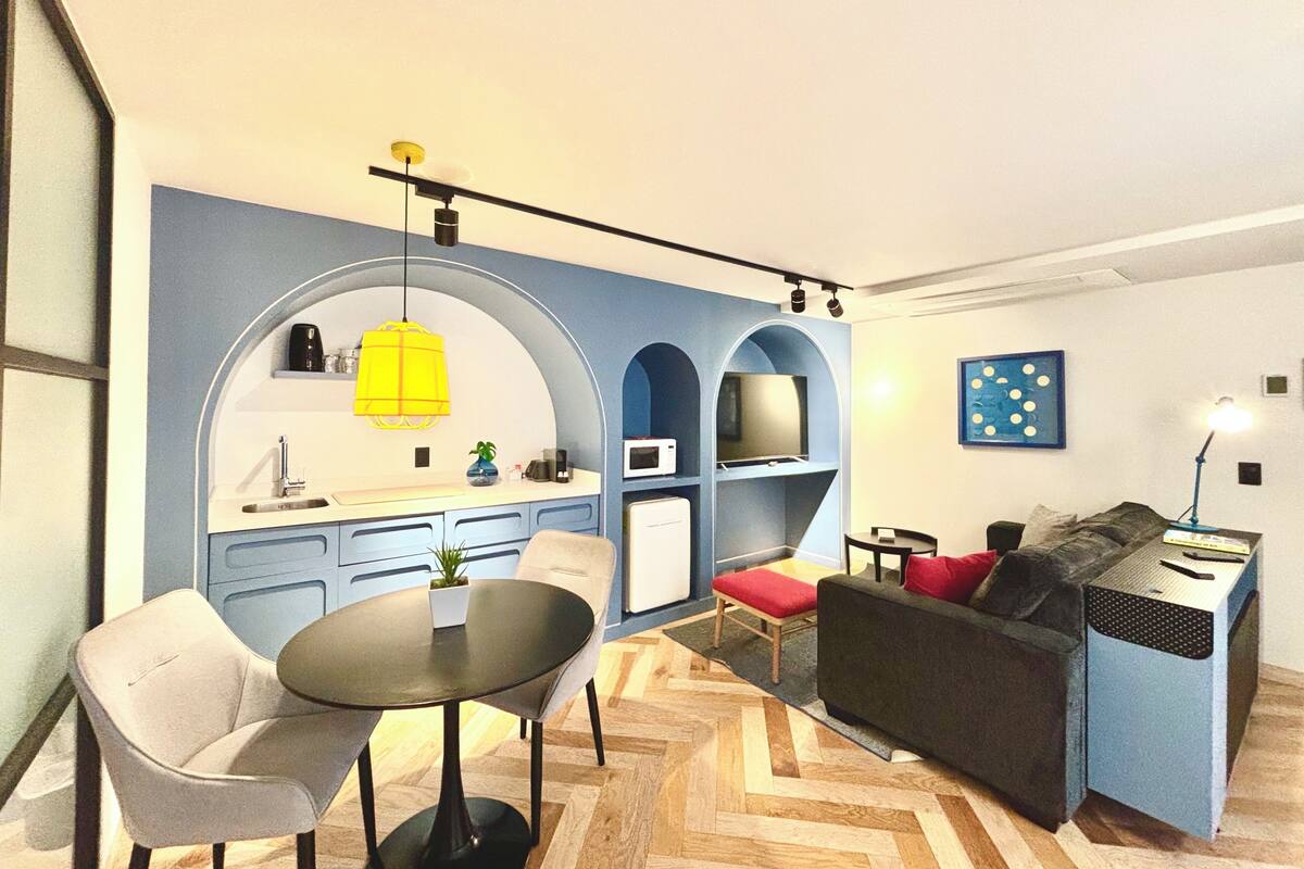 Un espacio habitable compacto con área de cocina, una mesa de comedor con sillas, un sofá y una mesita auxiliar.