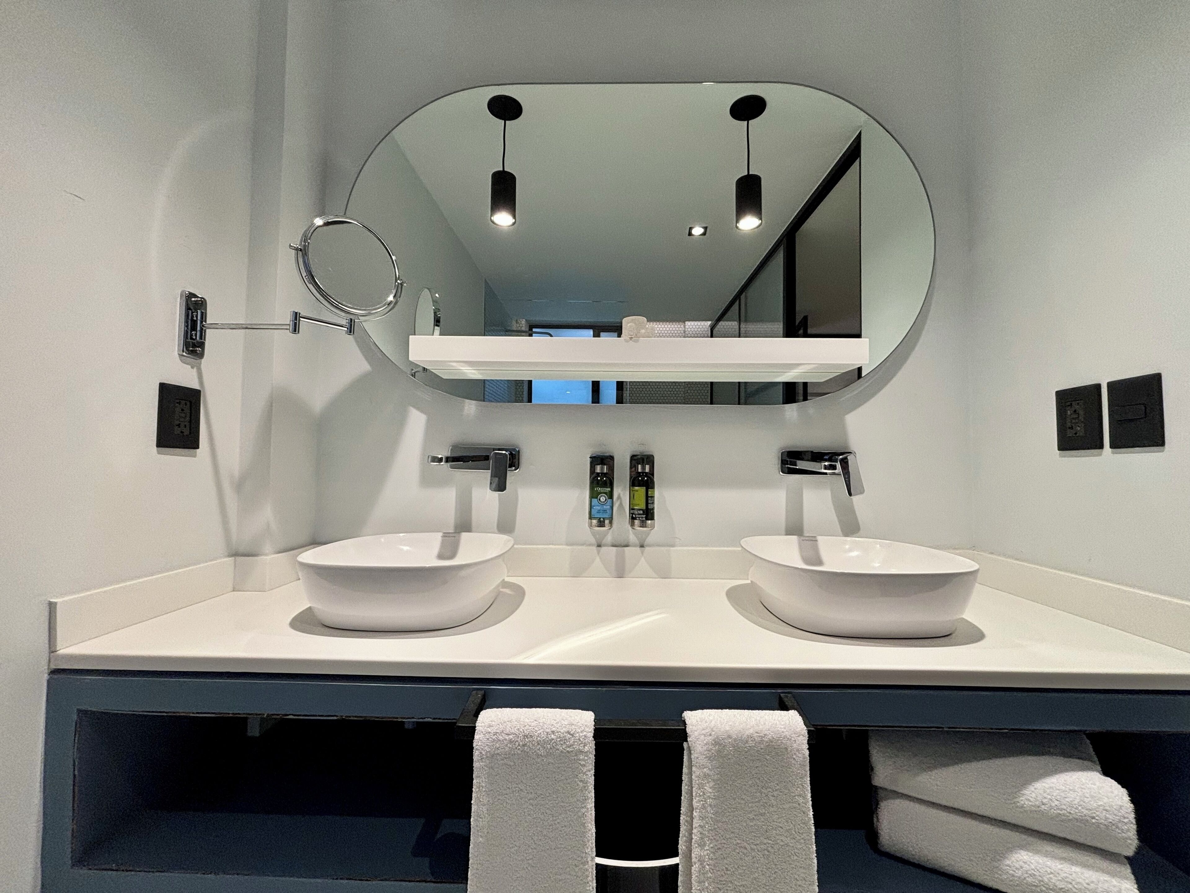 Un baño moderno con dos lavamanos blancos, un espejo grande y un perchero para toallas.