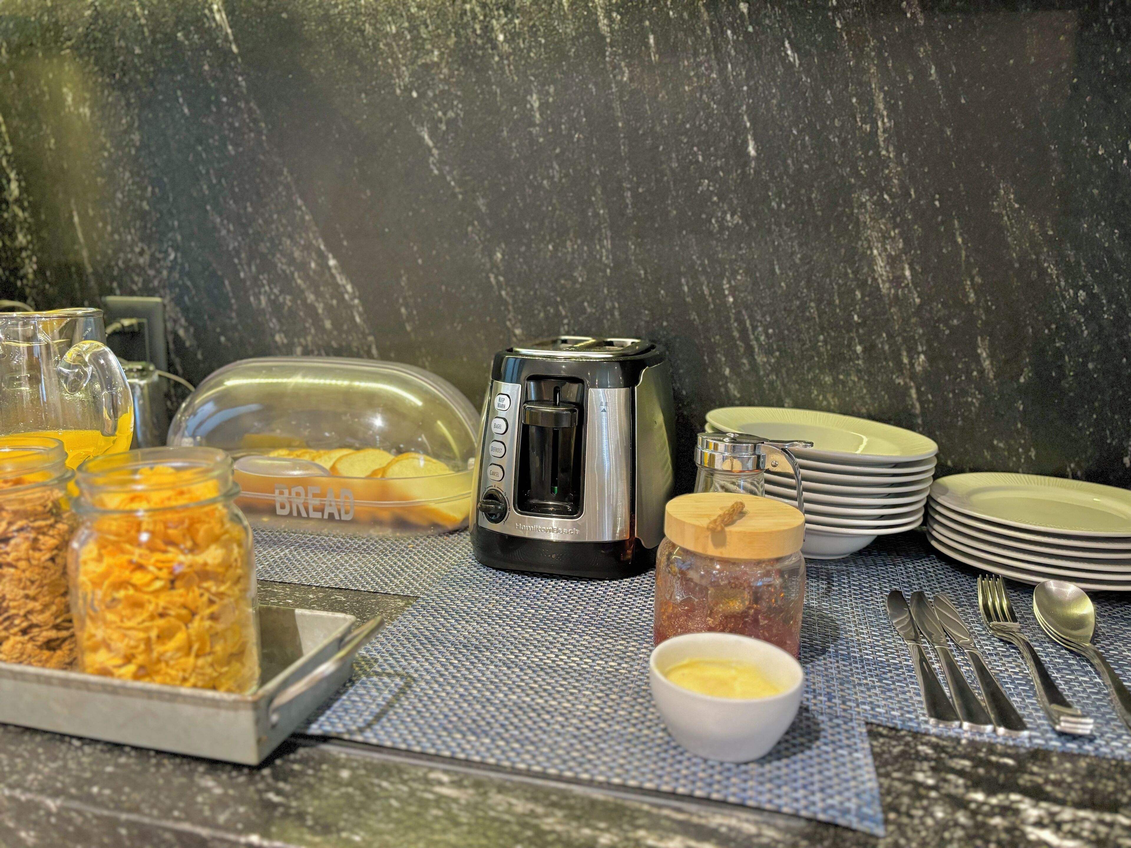 A breakfast buffet setup with a toaster, cereal, and condiments.