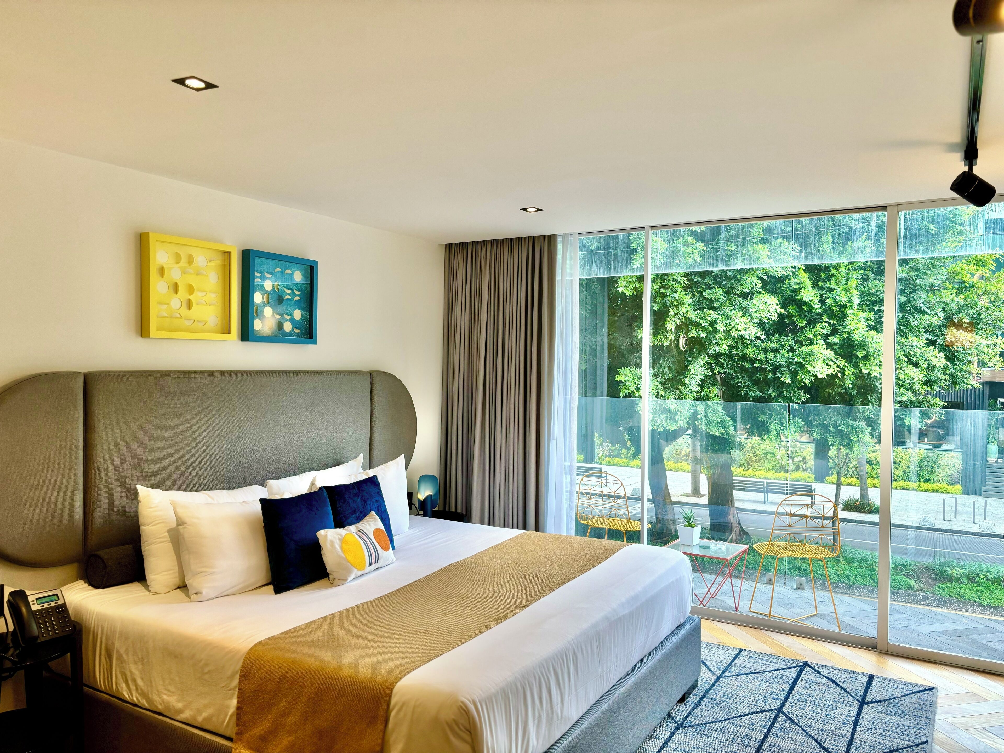 Habitación de hotel moderna con una cama grande, teléfono en la mesita de noche y vistas al área exterior a través de ventanales del suelo al techo.