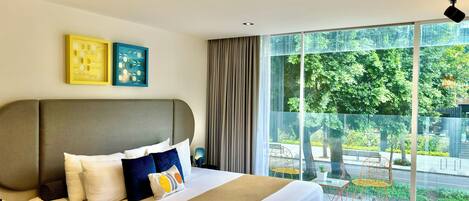 Habitación de hotel moderna con una cama grande, teléfono en la mesita de noche y vistas al área exterior a través de ventanales del suelo al techo.