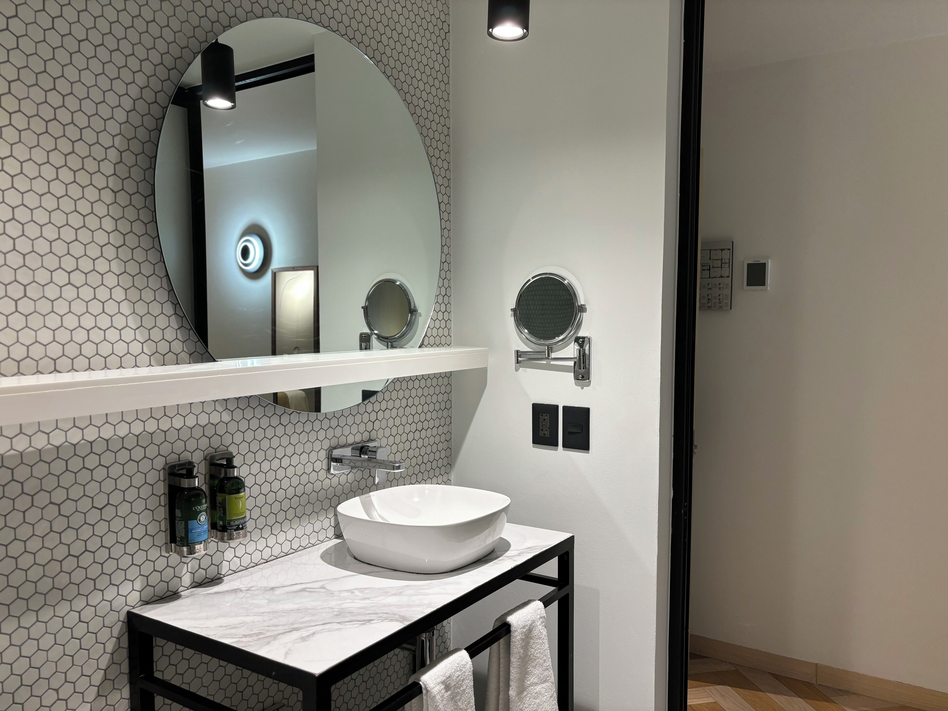 Un baño moderno con un lavamanos blanco, dos espejos redondos y un salpicadero de azulejos hexagonales.
