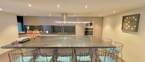 A modern kitchen with a large island, built-in appliances, and a dining area with metal chairs.