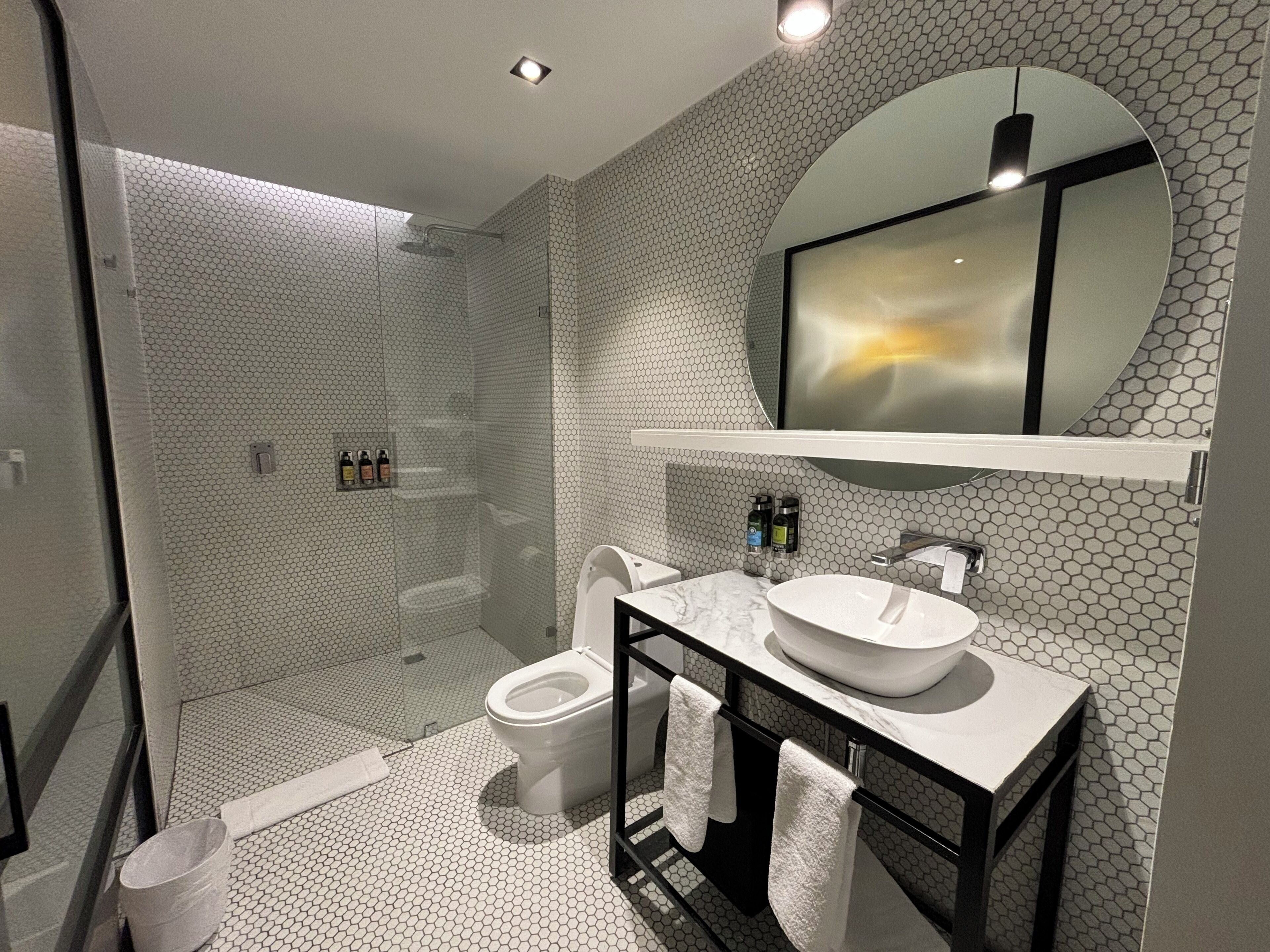 Uma casa de banho moderna com chão em mosaico hexagonal, um espelho grande sobre a pia e um chuveiro com cabine de vidro.