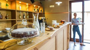 Een desserttafel met een taart op een glazen etagère, een bar met flessen op de planken, en een persoon die bij de bar staat.