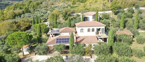 A villa with a tiled roof, surrounded by olive trees and a mountainous backdrop.