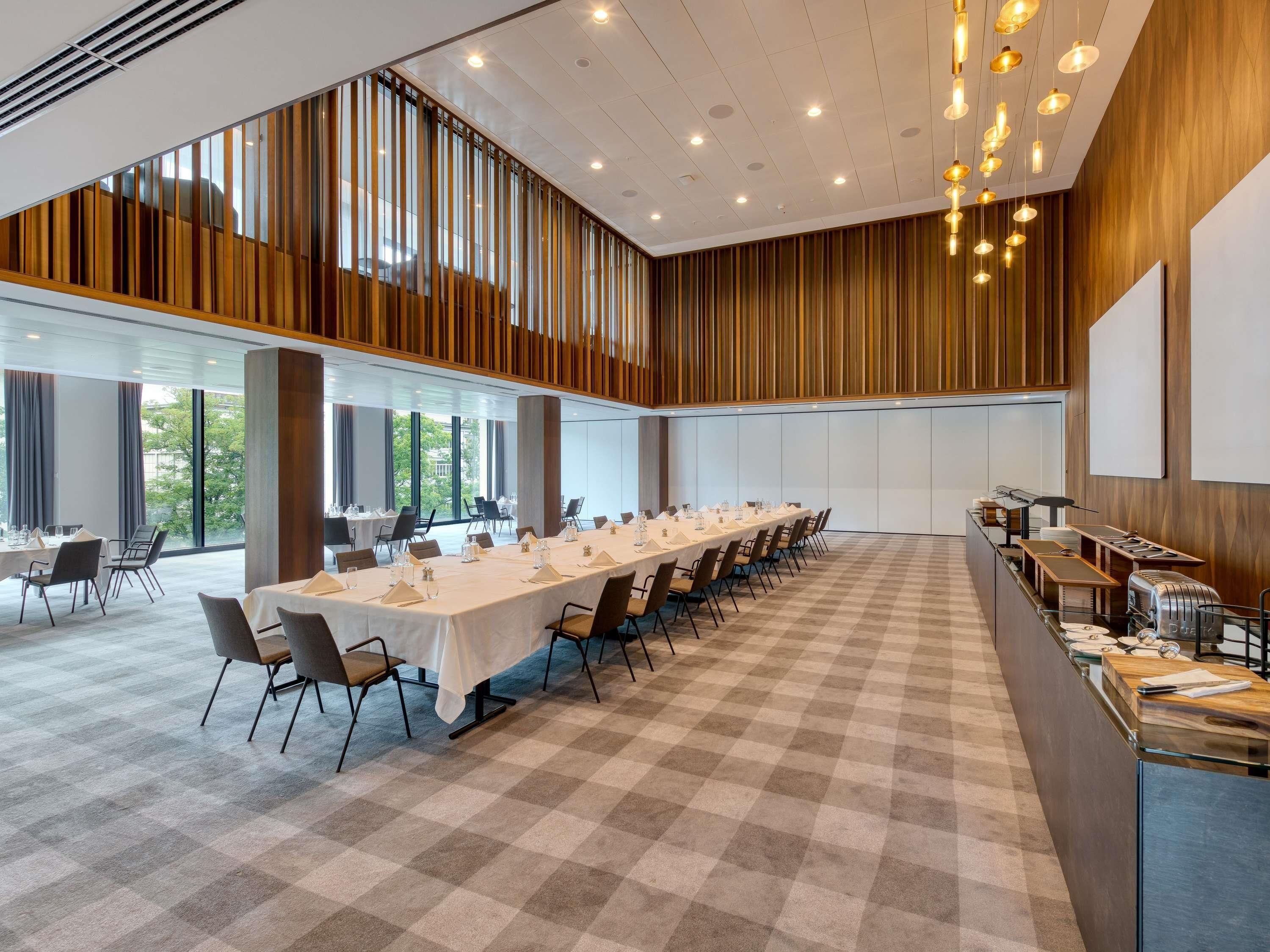 Un salón de conferencias con una larga mesa, sillas, una zona de buffet y ventanas grandes.