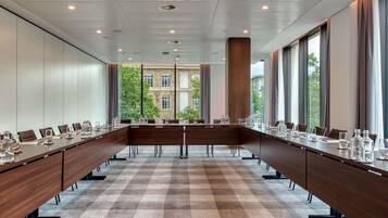 Een vergaderzaal met een lange tafel, stoelen en een geruit tapijt.